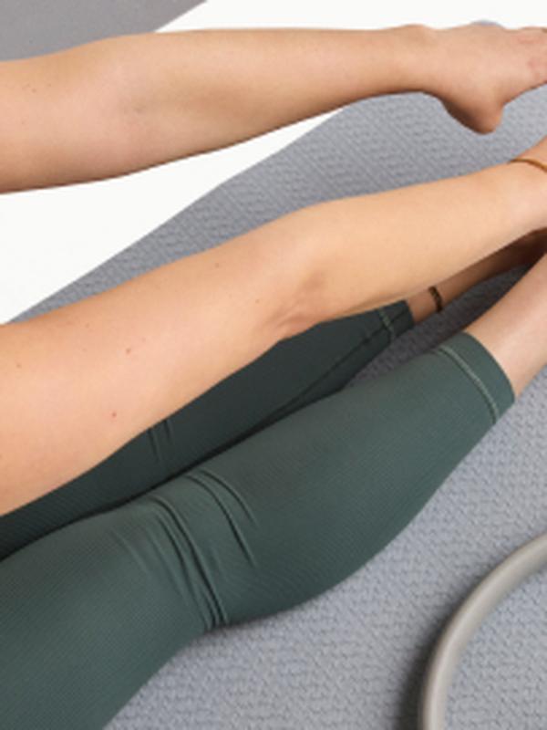 Woman stretching her legs on a yoga mat with a Pilates ring nearby.